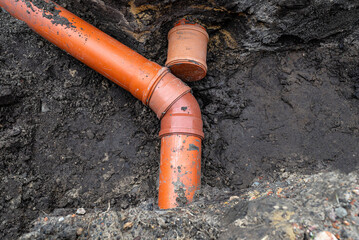 An orange plastic pipe from a septic tank with a diameter of 160 mm lying in a ditch, blind pipe...