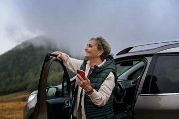 Beautiful happy gray-haired senior mature traveling by car using smartphone. Active pensioners concept