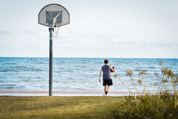 Hombre jugando a basquet en una pista frente al mar