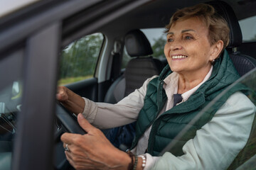 Beautiful happy smiling senior gray-haired mature woman driving a car