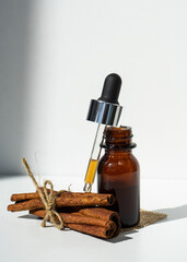 Obraz na płótnie Canvas A cinnamon stick and a bottle of essential oil on a white background with a space to copy. A bottle of natural essential oil, cinnamon sticks on a white table. Organic oil. Selective focus. 