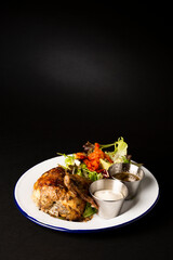 Roasted chicken on a white plate accompanied with a green salad over a black background