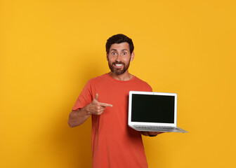 Handsome man with laptop on orange background