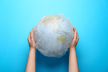 Woman holding globe packed in bubble wrap on turquoise background, top view. Environmental...