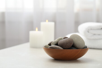 Fototapeta na wymiar Spa stones in wooden bowl on white table indoors. Space for text