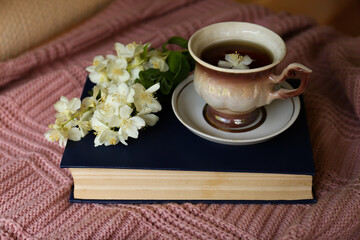 Cup of aromatic tea, beautiful jasmine flowers and hardcover book on pink fabric