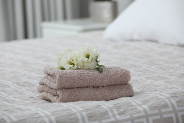 Stack of clean towels and Eustoma flowers on bed indoors