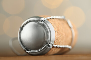 Sparkling wine cork with muselet cap on table against blurred festive lights, closeup