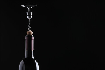 Opening wine bottle with corkscrew on dark background, closeup. Space for text - obrazy, fototapety, plakaty