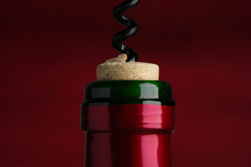 Opening bottle of wine with corkscrew on burgundy background, closeup
