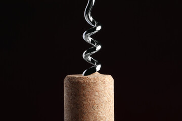 Corkscrew with cork against dark background, closeup