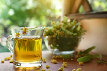 Glass cup of aromatic tea with linden blossoms on wooden table against blurred background, space for text