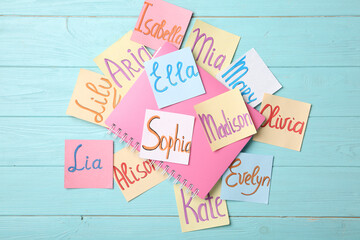 Paper notes with different baby names and notebook on light blue wooden table, flat lay