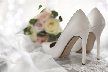 Pair of white high heel shoes, veil and wedding bouquet on light background
