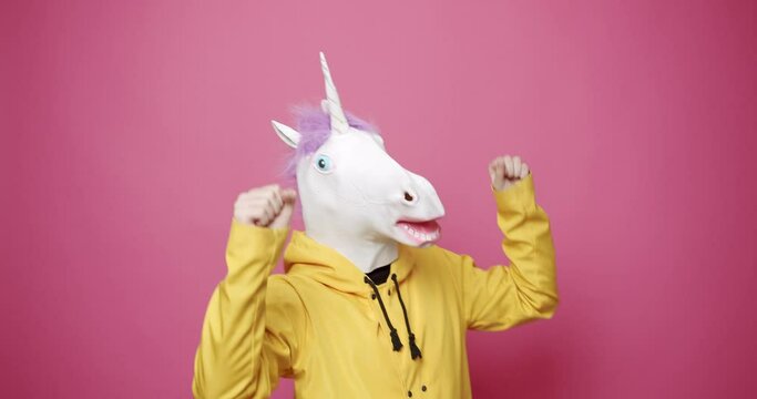 Man with unicorn mask making funny gestures. Man with Unicorn Mask. Fun and happiness concept. Funny Guy in Yellow Suits Dance with Unicorn Mask, Man having fun on isolated pink Background. 