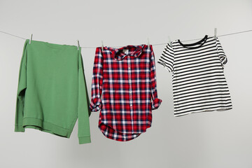 Different shirts drying on laundry line against light background
