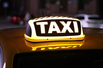 Taxi car with yellow sign on city street at night, closeup