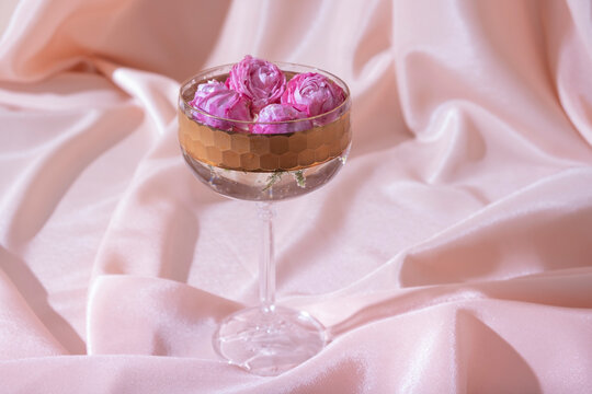 Bokal glass with roses in champagne on fabric folds background. Creative still life in pastel pink colors