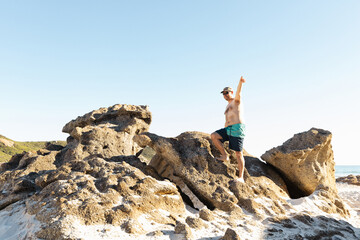 Obraz premium a father wearing board shorts and no shirt standing on top of rocks at a beach
