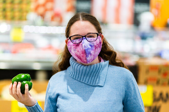 Woman in grocery store holding fresh capsicum fruit and wearing a covid face mask