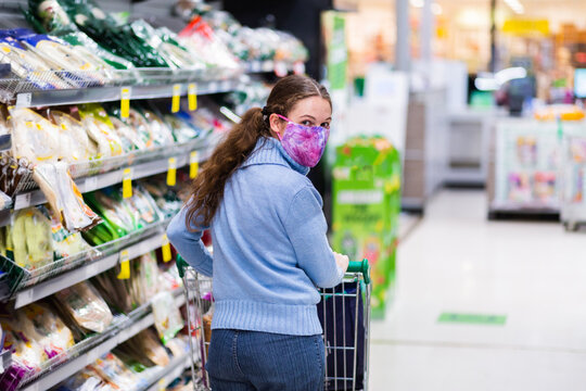 Young female person at the supermarket wearing a face mask while shopping due to coronavirus