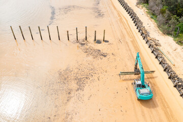 Aerial view of a colourful digger carrying poles along a sandy beach