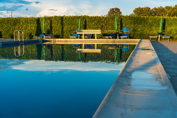 The blue sky is reflected on the surface of the outdoor pool, the summer beautiful pool in the hotel, comfortable summer vacation in Italy, the play of reflections on the surface of the water