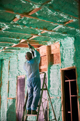 Male builder insulating wooden frame house. Man worker spraying polyurethane foam inside of future...