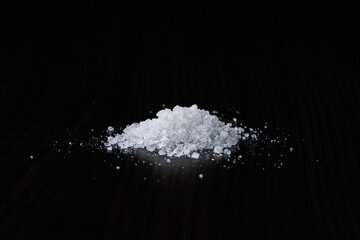 A pile of coarse-grained sea salt on a black table background. Selective focus. Close-up.