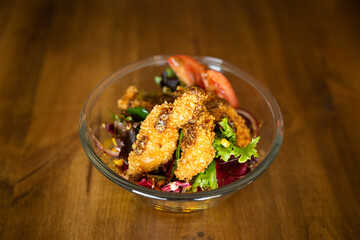 Green salad with chicken fingers on top in a big bowl on a wooden table