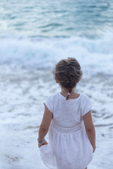 Petite fille enfant de dos qui regarde l'océan les pieds dans l'eau