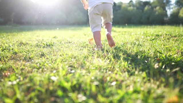 baby running in the park with bare feet. close-up of the kid leg runs in the summer on the green grass at sunset in the park. happy family kid concept. baby running and playing in the park dream