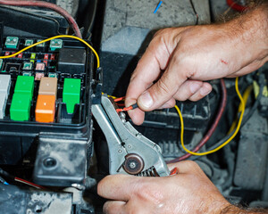 The master cleans the insulation from the wires under the hood of the car. The concept of repairing...