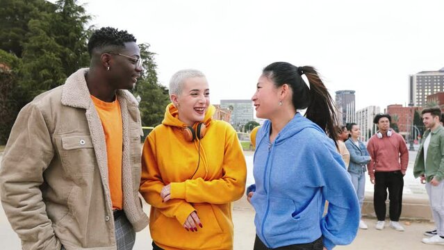 Group Of Three Multiethnic Teenage Students Standing Outside College Building tlking bout homeworks, at the background five friends laughing.