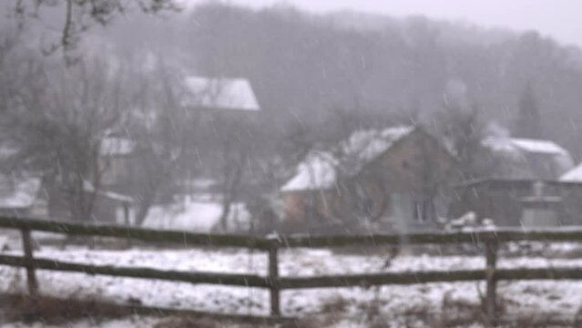 Snow is falling on a blurred background of houses.