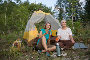  two middle aged women friends relaxed in a tent and hiking in nature and spending time together. travel tourism concept. Outdoor activities on weekends. Amazing chill moment