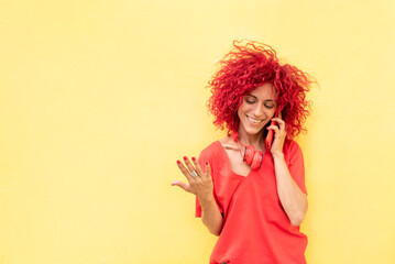 a happy young woman with red afro hair talks on the smartphone on a yellow background