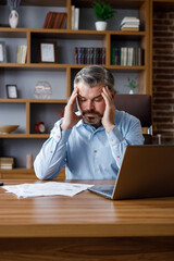 Depressed adult man calculating monthly expenses. Mad gray-haired businessman feels frustrated about high bills, bank debt, tax invoice, credit payment. Financial problems, crisis, bankruptcy.