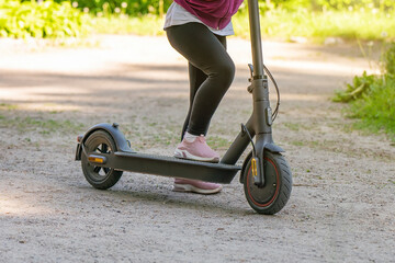 Little girl rides an electric scooter on a dirt road in the park