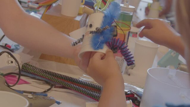 Girl placing colorful feather on decorated cup during arts and crafts