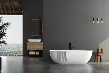 Stylish gray bathroom interior with concrete floor, window with city view, dark wall, white bathtub, and sink with vertical mirror and wooden vanity. 3d rendering copy space
