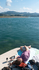 Hombre tumbado junto a lago leyendo libro electr&oacute;nico