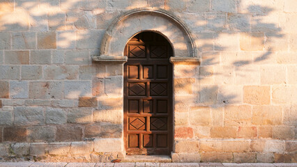 Puerta de madera tallada en arco en fachada de piedra 
