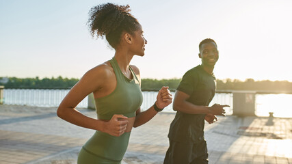 Black sportsman and sportswoman run on promenade © Svitlana