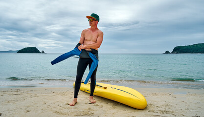 A man puts on a wetsuit on the beach and is going for a walk on the sea on a SUP board. Active recreation.