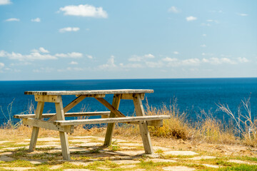 A lonely bench with a table on the edge of a cliff by the sea. Summer sun.