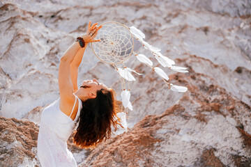 Beautiful girl in white dress holding a dreamcatcher in her hands.