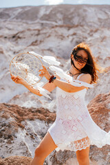 Beautiful girl in white dress holding a dreamcatcher in her hands.