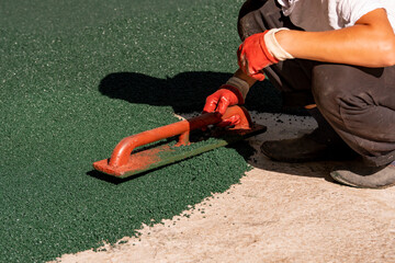 A worker applies a rubber coating to a concrete surface prepared for coating. Rubber crumb obtained...