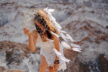 Beautiful girl in white dress holding a dreamcatcher near with her face.